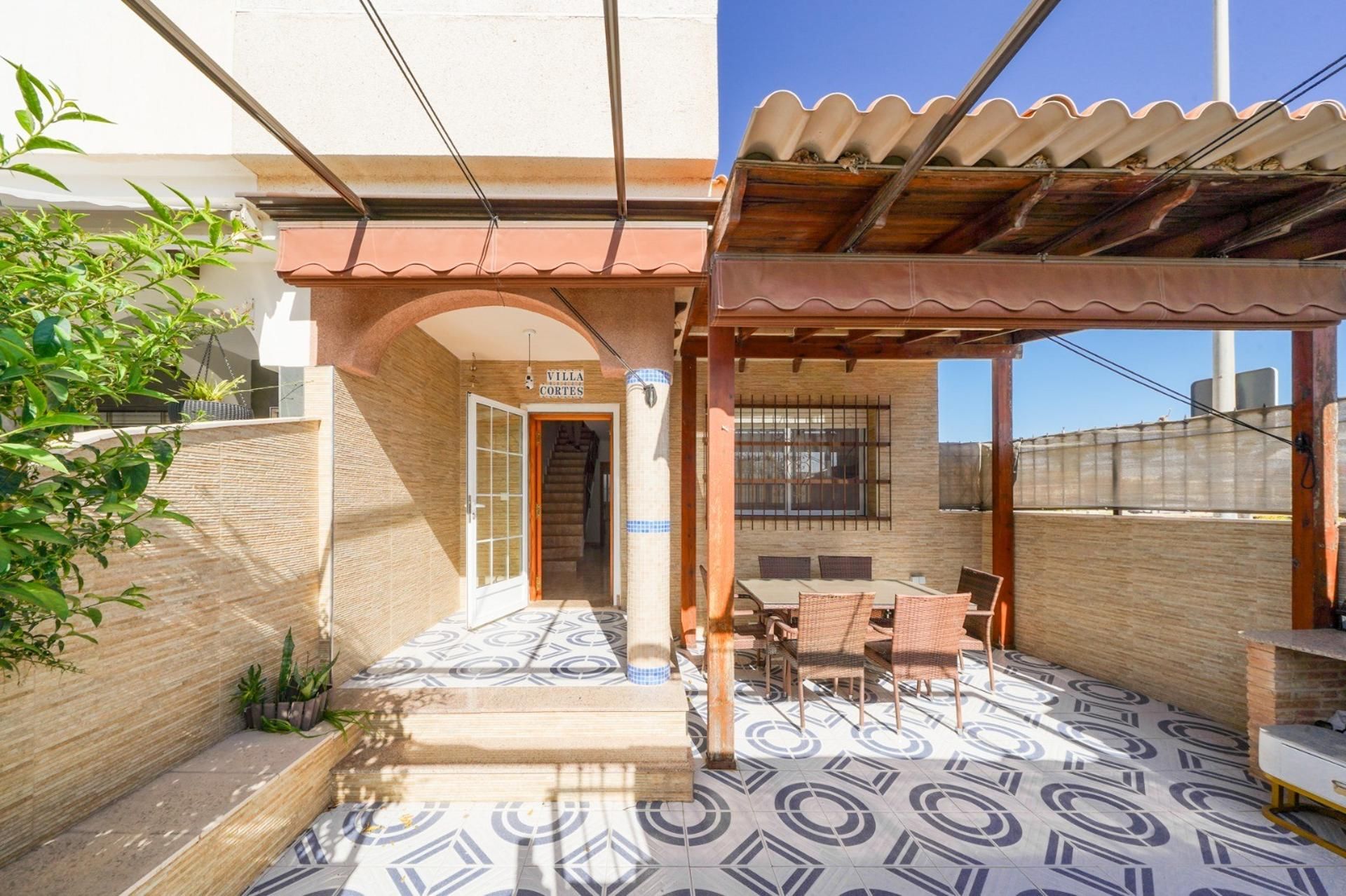 A covered patio area with a tiled floor, a wooden pergola, and a sign that reads 'VILLA CORTES'.
