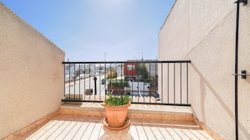 A balcony with a potted plant, a metal railing, and a view of a street with buildings.