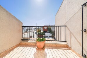 A balcony with a potted plant, a metal railing, and a view of a street with buildings. - 4-bed Villa, Sleeps 8, Pets Ok & 10 min to Beach (Los Alcazares)