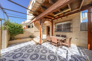 Un patio cubierto con suelo de baldosas, una mesa con sillas y vista a un edificio con el letrero 'Villa Cortes'.