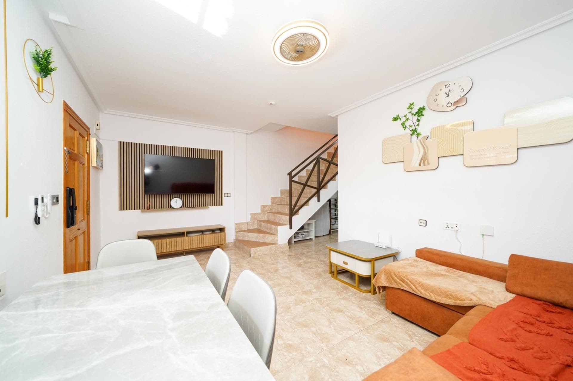 Una sala moderna con un televisor de pantalla plana, un comedor con una mesa de mármol, una escalera y un sofá.
