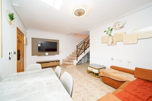 En moderne stue med et fladskærms-tv, et spiseområde med et marmorbord, en trappe og en sofa.