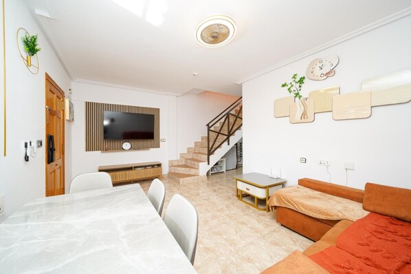 A modern living room with a flat-screen TV, a dining area with a marble table, a staircase, and a sofa. - 4-bed Villa, Sleeps 8, Pets Ok & 10 min to Beach (Los Alcazares)