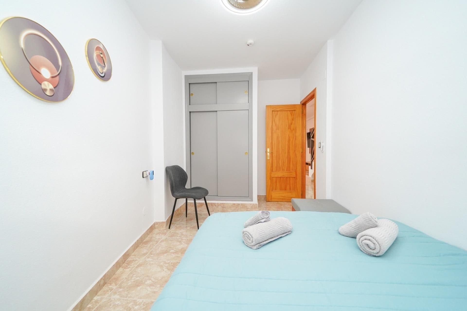 Ein Schlafzimmer mit einem Bett, einem Sessel, einer Holztür und einer Wandleuchte.
