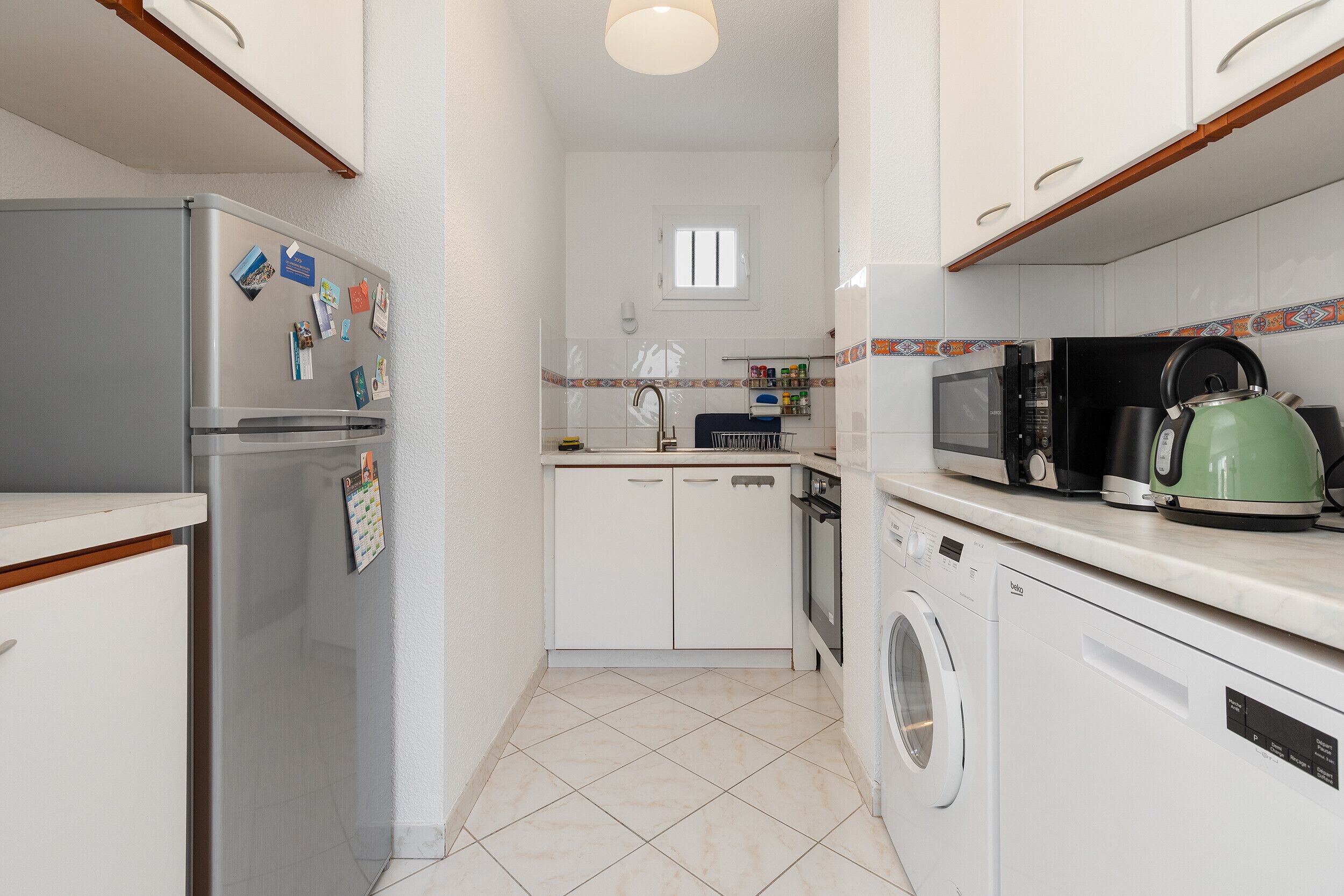 A compact kitchen with a refrigerator, microwave, kettle, and washing machine.