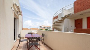 A balcony with a table and chairs, a red door, and a staircase.