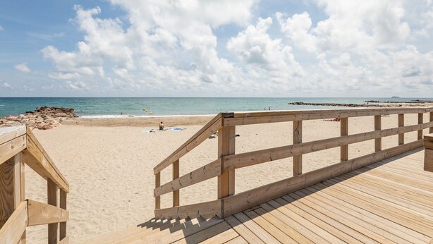 A wooden boardwalk leading to a sandy beach with a clear sky and calm sea.
