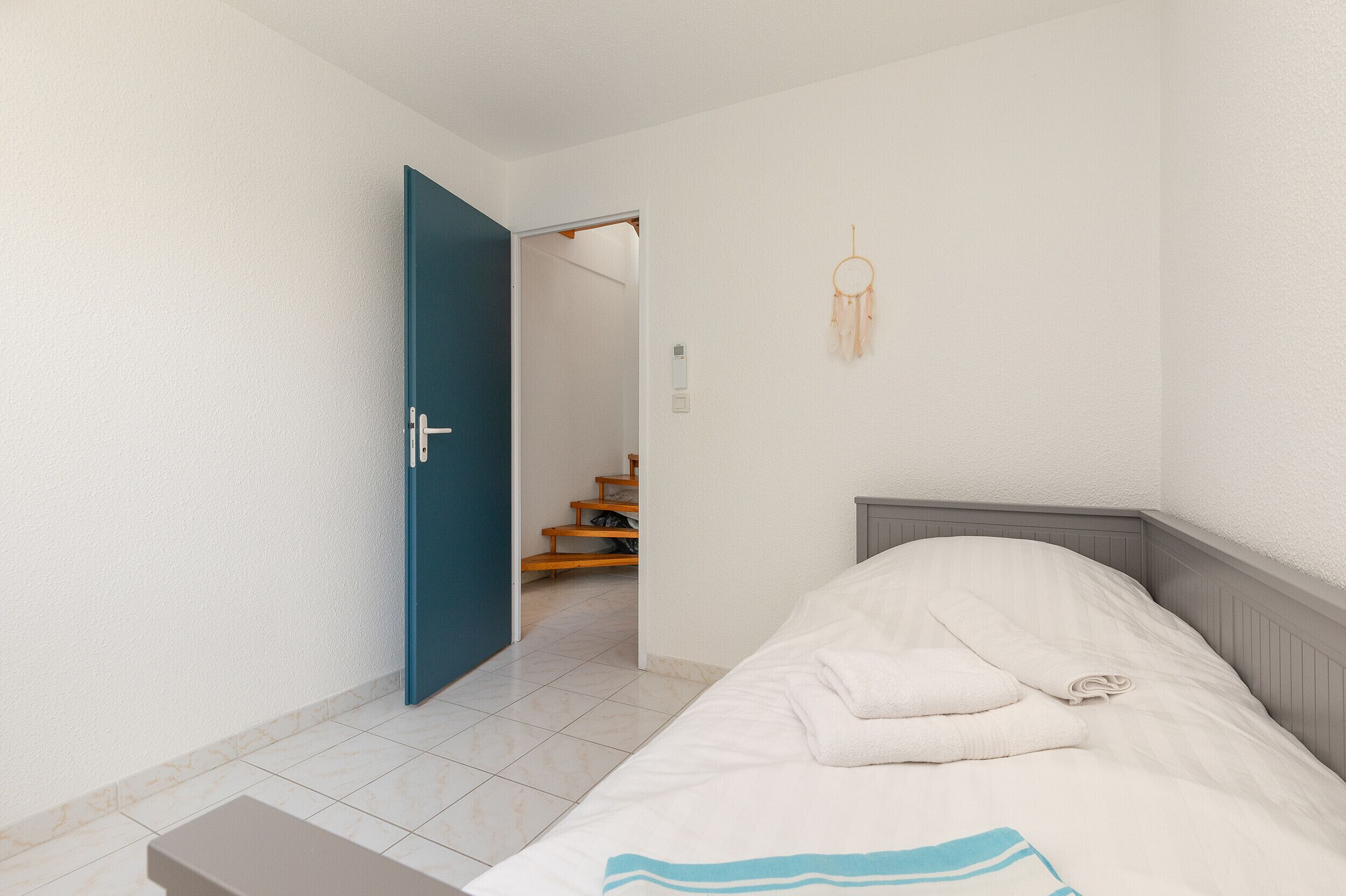 A bedroom with a bed, a blue door, a dreamcatcher, and a staircase leading to another room.