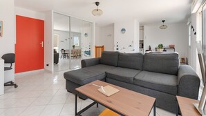 A modern living room with a grey sectional sofa, a wooden coffee table, and a bright red door.