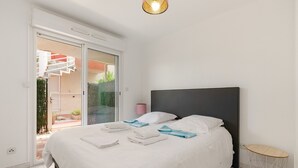 A bedroom with a bed, a small round table, a nightstand, and a sliding glass door leading to a balcony.