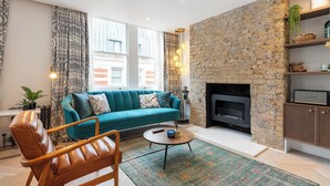 A living room with a teal sofa, a leather armchair, a round coffee table, and a fireplace with a stone wall.