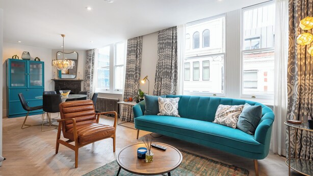 A modern living room with a teal sofa, wooden coffee table, and a dining area with a blue cabinet and black chairs.