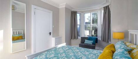 Quarto com cama grande, janela com cortinas, mesa de cabeceira e abajur.