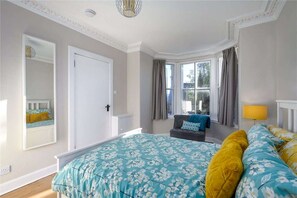 Un dormitorio con una cama grande, una ventana con cortinas, una mesita de noche y una lámpara.