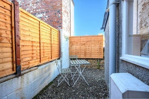 A narrow outdoor space with a wooden fence, a small table, and a window. - Lade Braes No 35 | St Andrews (St Andrews)