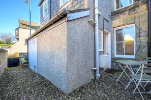 Un edificio de fachada texturizada, con un pequeño espacio al aire libre con sillas metálicas y suelo de grava.