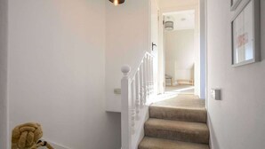 Un escalier avec une rampe blanche et des marches recouvertes de moquette, menant à une pièce dotée d’une porte.