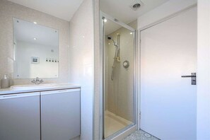 Un baño moderno con ducha envuelta en vidrio, un espejo grande y un tocador blanco.