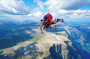 A person skydiving over a mountainous landscape with visible valleys and a body of water below.