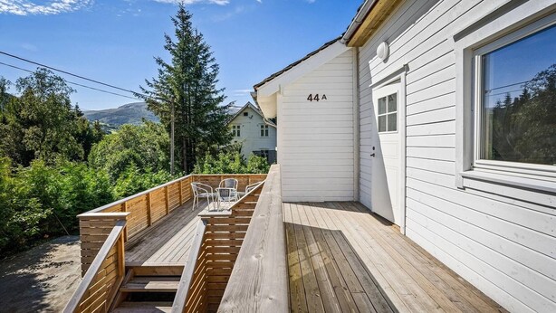A wooden deck with a built-in bench and a small table, adjacent to a white house with the number 44A. - Entire Single-family Home - Centrally Located in Voss (Voss)