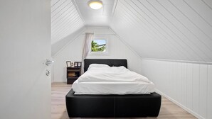 A bedroom with a black bed, white walls, a small window with curtains, and a ceiling light. - Entire Single-family Home - Centrally Located in Voss (Voss)