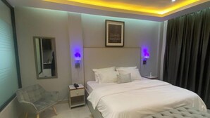 Un dormitorio moderno con una cama grande, lámparas de noche, una silla y un banco.