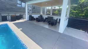 Un espacio al aire libre techado con piscina, asientos y vistas de los edificios circundantes.