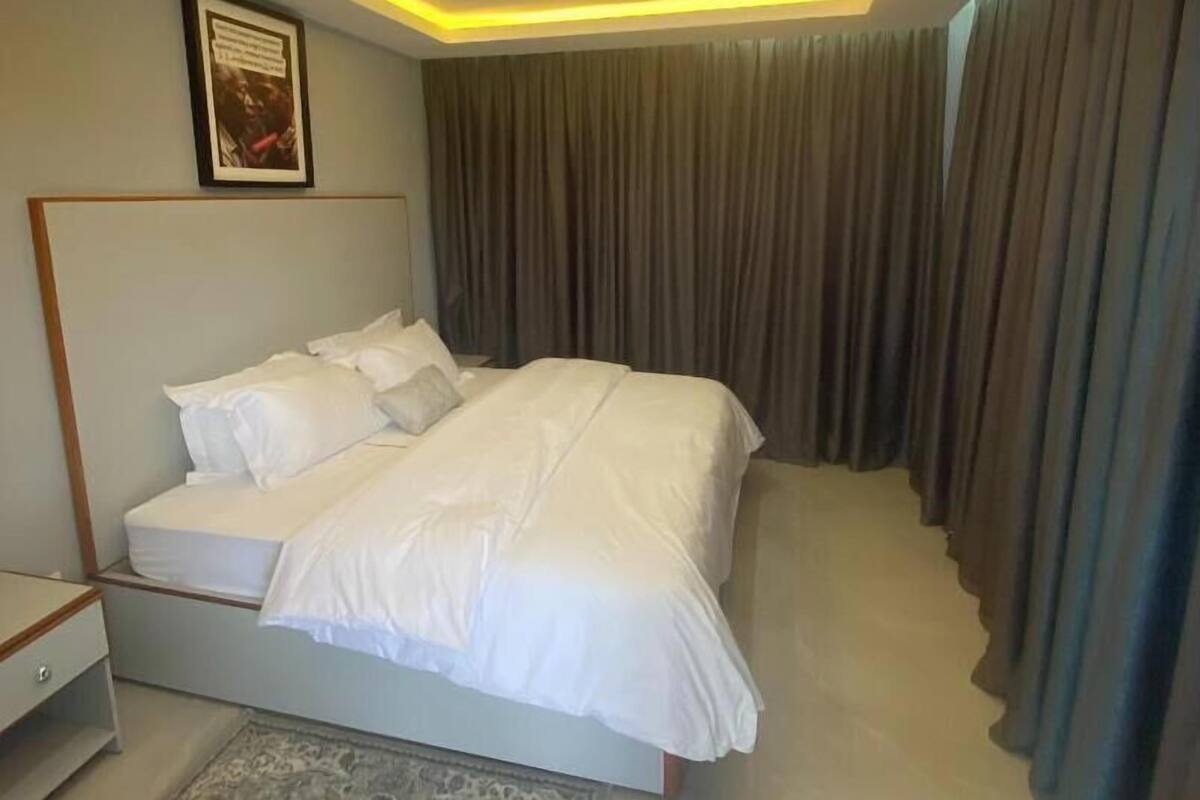 A modern bedroom with a large bed, a nightstand, a framed picture on the wall, and a patterned rug.