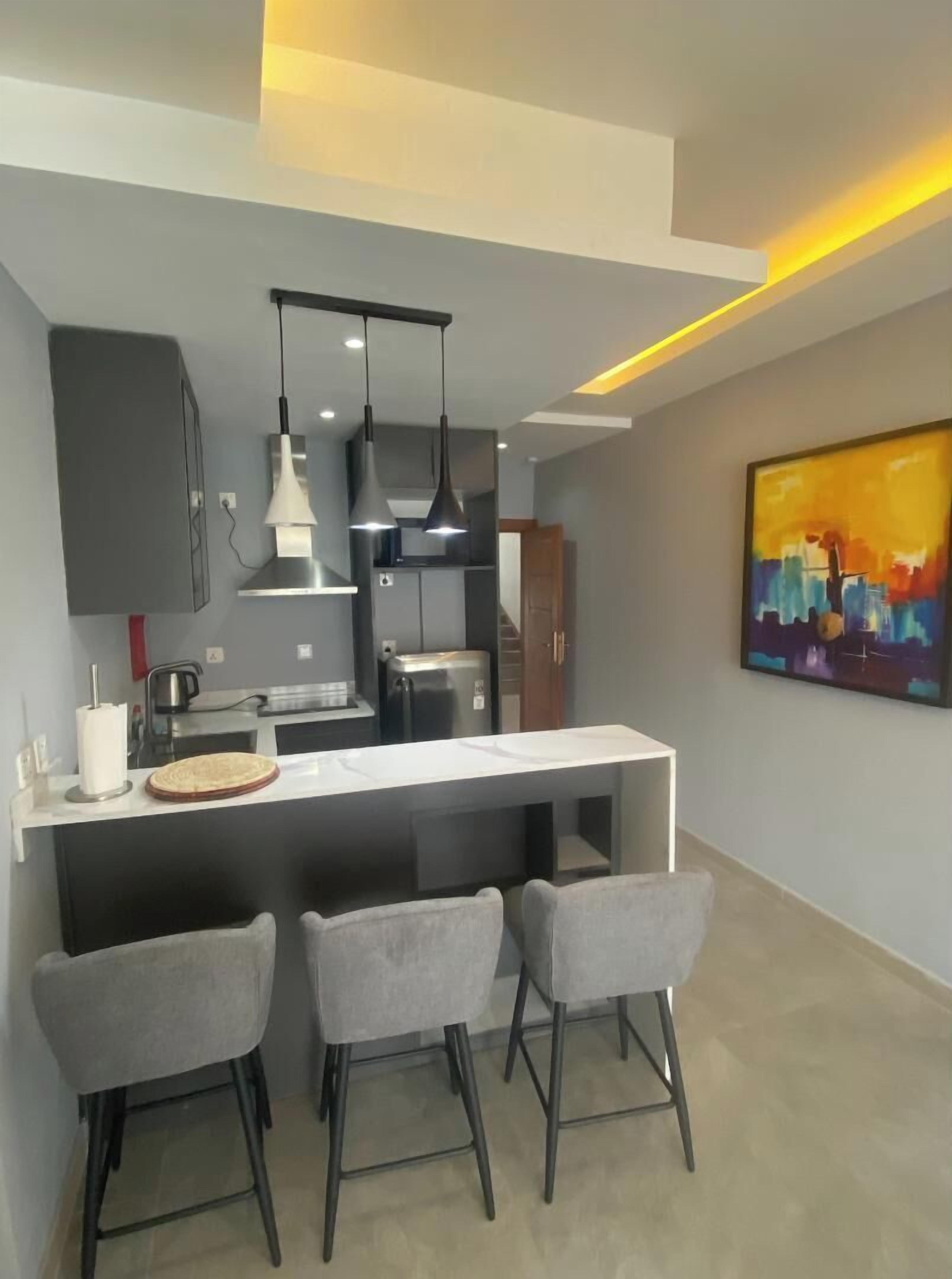 A modern kitchen with a central island, bar stools, pendant lighting, and a colorful abstract painting on the wall.