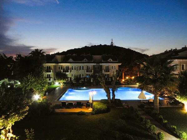 A hotel with a swimming pool, palm trees, and a large building in the background.