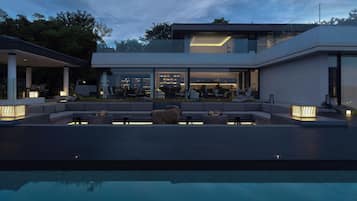 Una casa moderna con piscina, mobiliario exterior e interior bien iluminado.