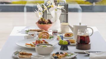 A table set with breakfast items including croissants, fruit, and tea, overlooking a lake.