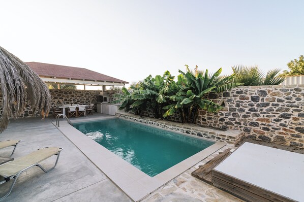 A swimming pool with stone walls and a thatched roof structure.