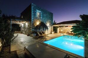 A stone building with a swimming pool, outdoor seating, and a covered patio area.