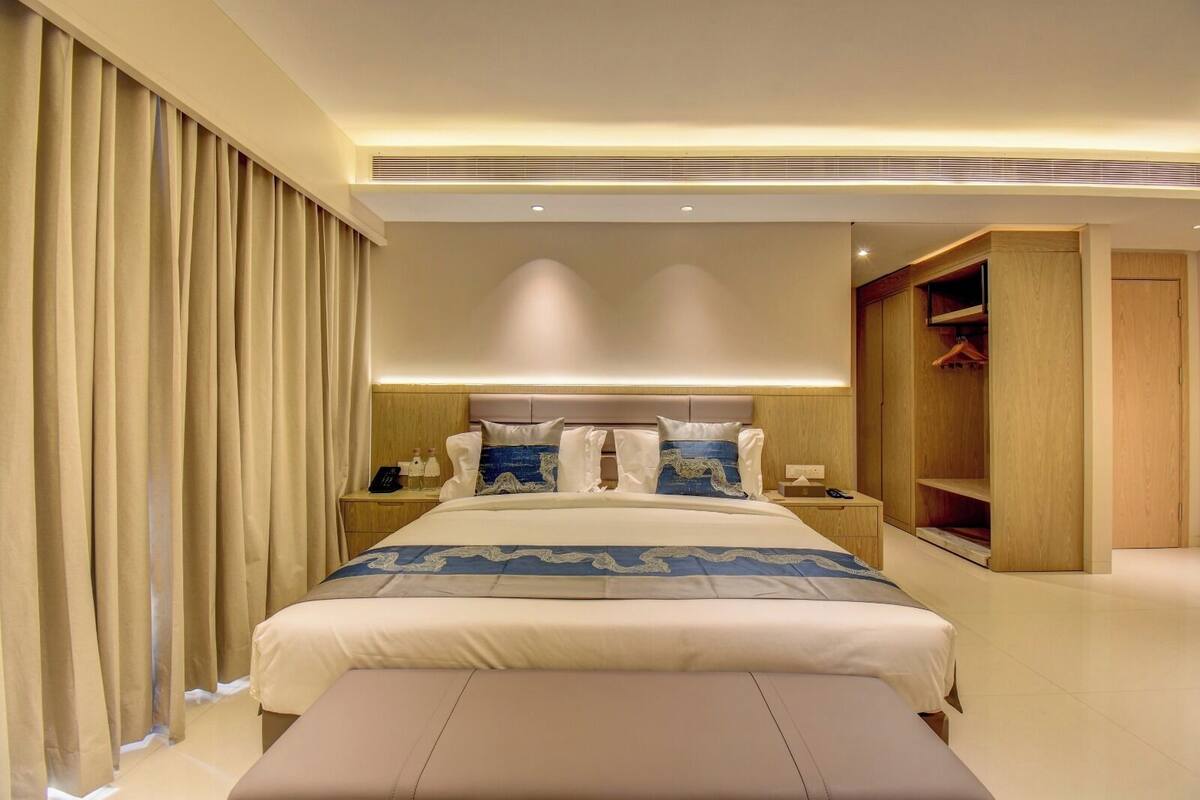 Een moderne hotelkamer met een groot bed, nachtkastjes, een kledingkast en een bankje.