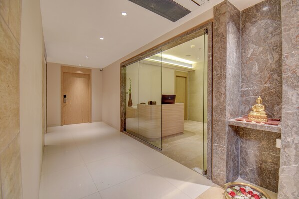 A modern hotel lobby with a marble reception desk, a glass partition, and a Buddha statue on a shelf.