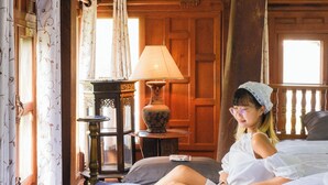 A bedroom with a wooden ceiling, a bed with white bedding, a nightstand with a lamp, and a window with curtains. - Ban MaeBo Local Stay (Mae Rim)