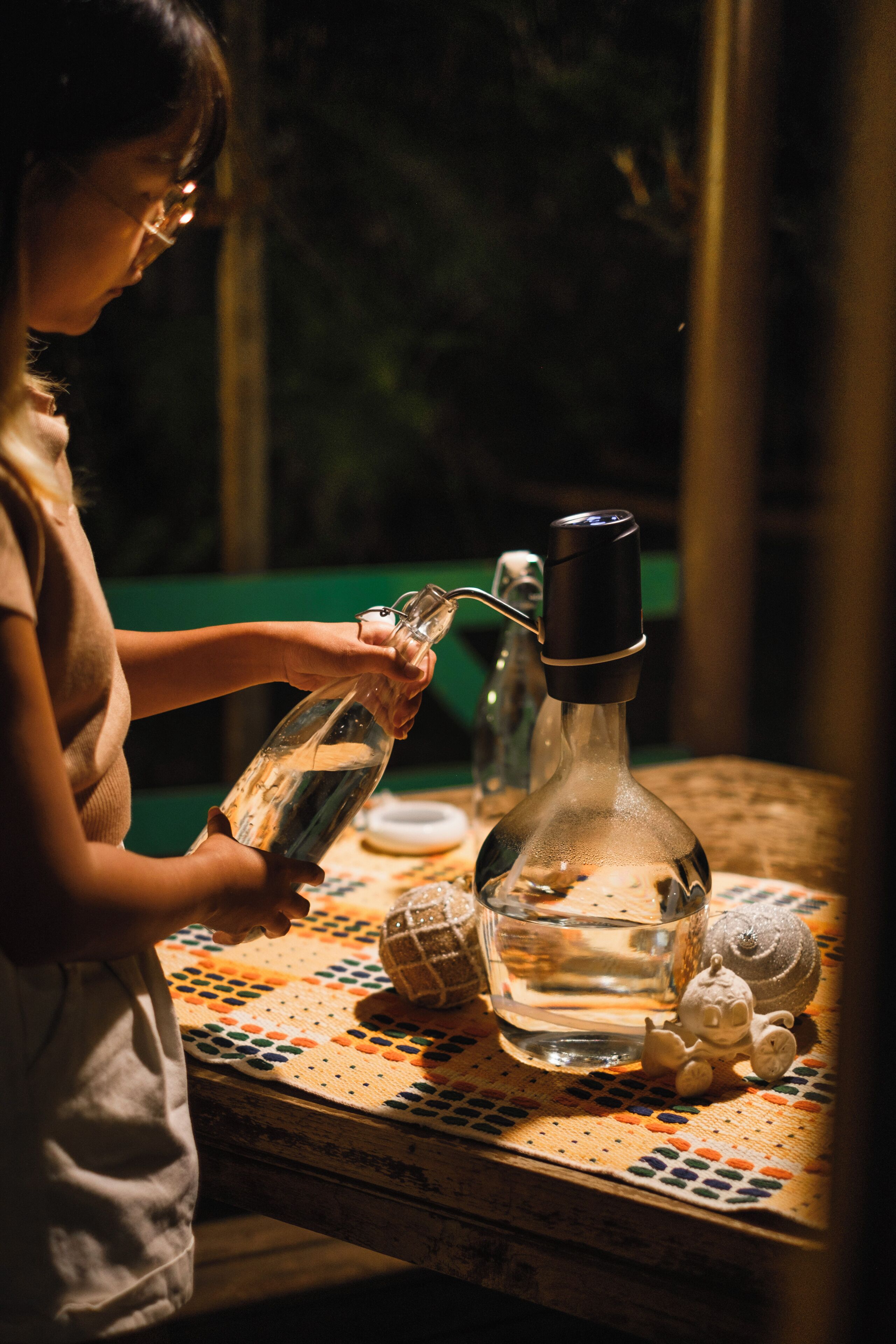 A child pouring water from a glass bottle into a larger bottle with a black cap.