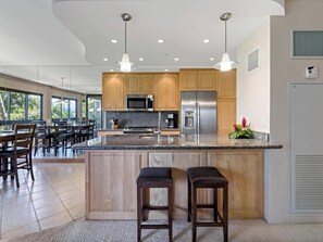 A modern kitchen with granite countertops, stainless steel appliances, wooden cabinets, and pendant lighting.