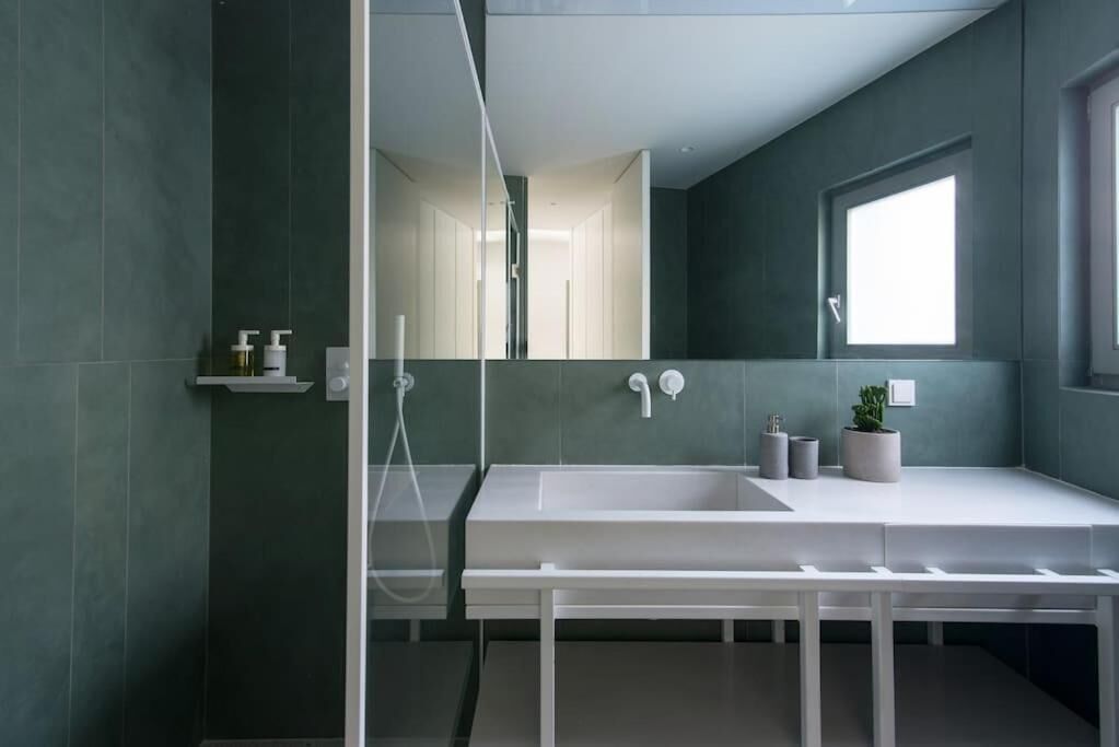 A modern bathroom with a large mirror, a white sink, and a window.