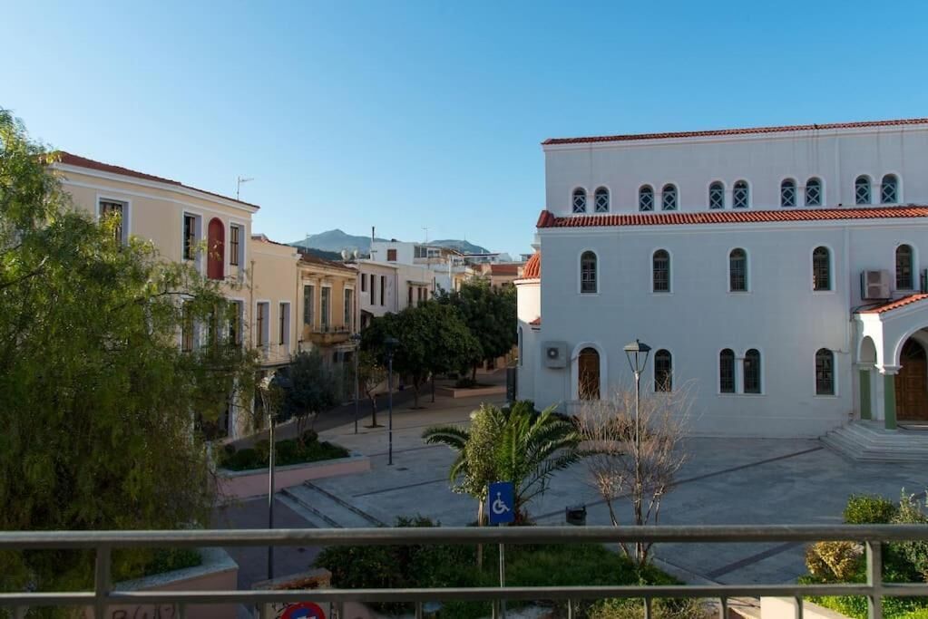 A building with a white facade and red-tiled roof, surrounded by greenery and other buildings.