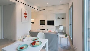 A modern kitchen with white cabinetry, a dining table with plates of food, and a TV mounted above the counter. - Main Suite (Rethymno)