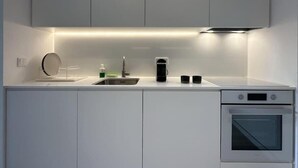 A modern kitchen with white cabinets, a stainless steel sink, a coffee maker, and an oven. - Main Suite (Rethymno)