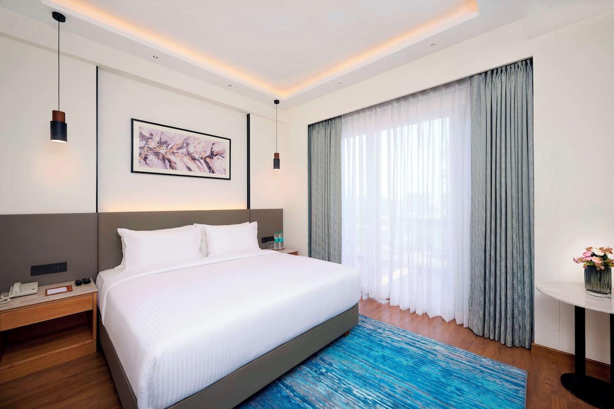 Una camera d'albergo con un letto grande, un comodino con telefono e lampada, un quadro appeso alla parete e una finestra con tende.