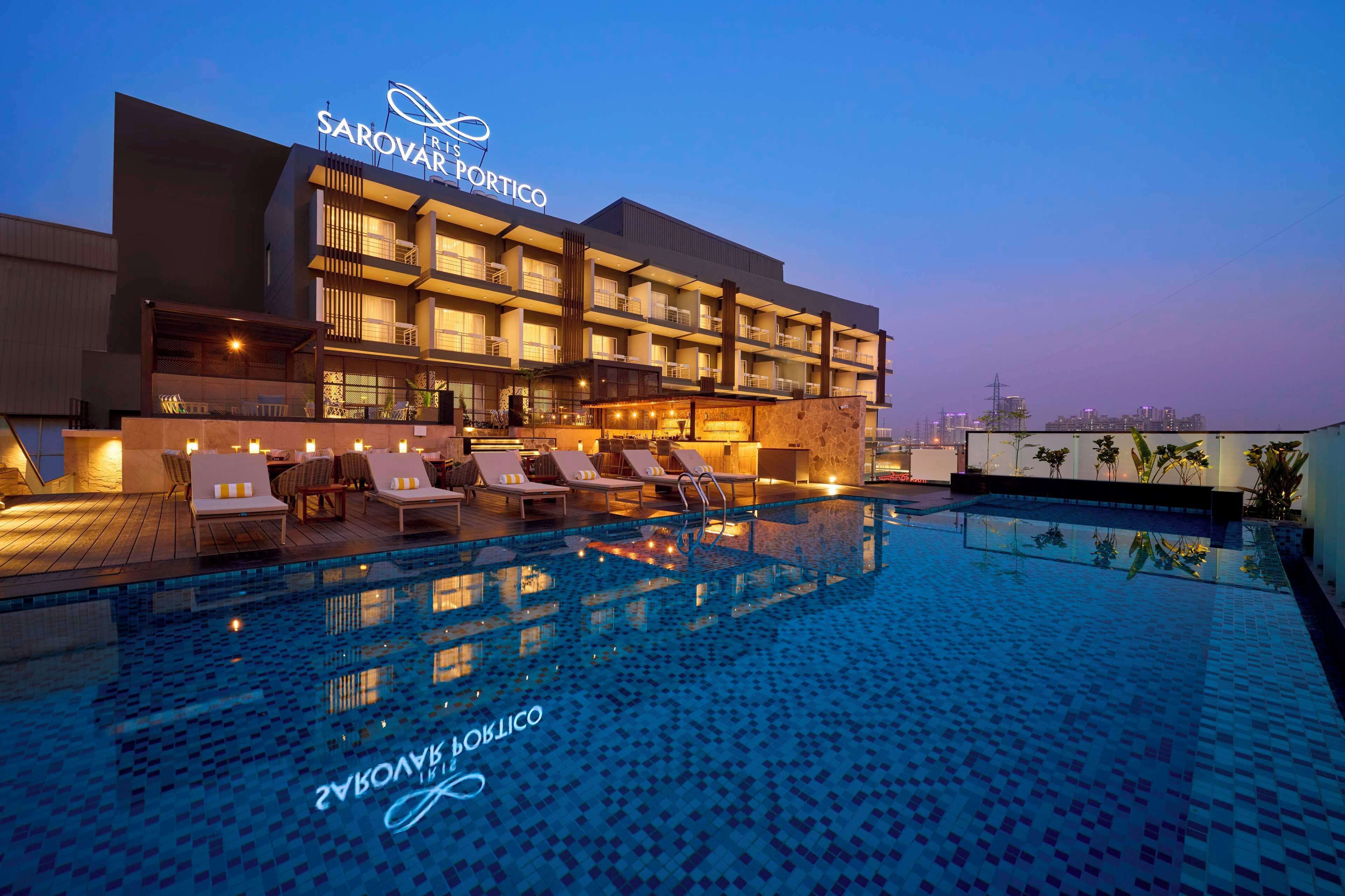 Hotel com piscina, espreguiçadeiras e fachada bem iluminada.