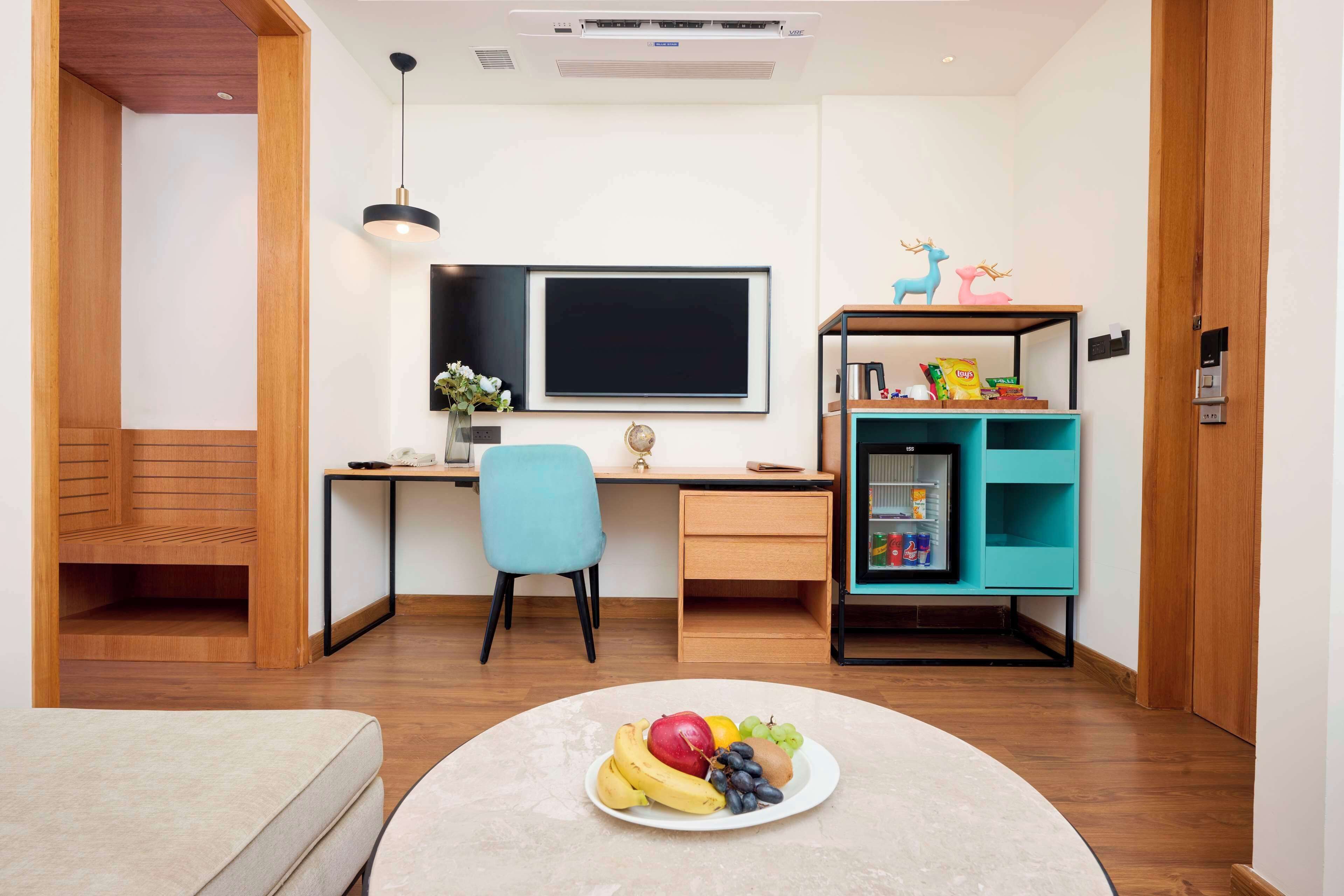 A modern room with a wooden desk, a blue chair, a teal shelf, and a fruit plate on the table.