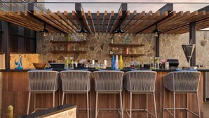An outdoor bar area with a stone wall, wooden pergola, and wicker bar stools. - Iris Sarovar Portico Sector 85 Gurugram (Gurugram)