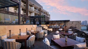 An outdoor patio with wicker furniture, a bar area, and a view of a modern building. - Iris Sarovar Portico Sector 85 Gurugram (Gurugram)
