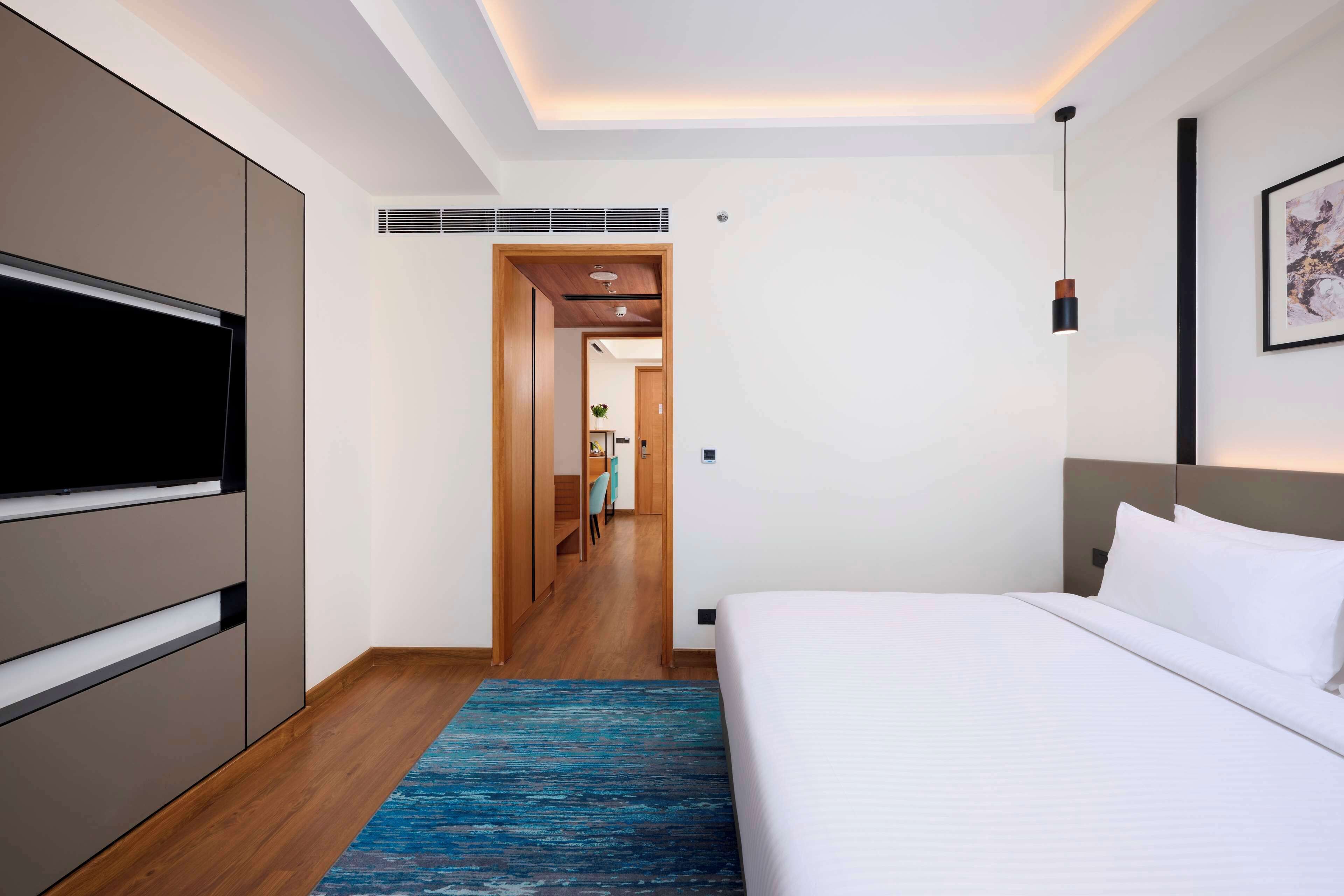 A modern hotel room with a large bed, a flat-screen TV, and a walk-in closet.