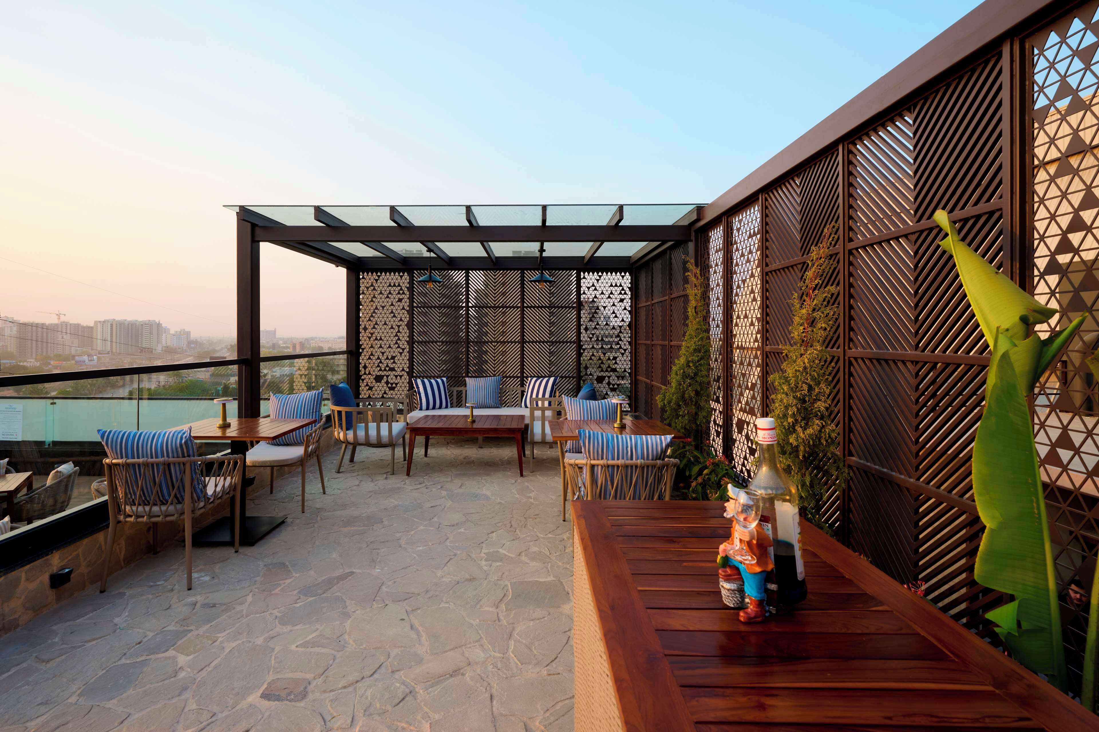 Un patio al aire libre con suelo de piedra, mobiliario de madera y una pérgola de vidrio.